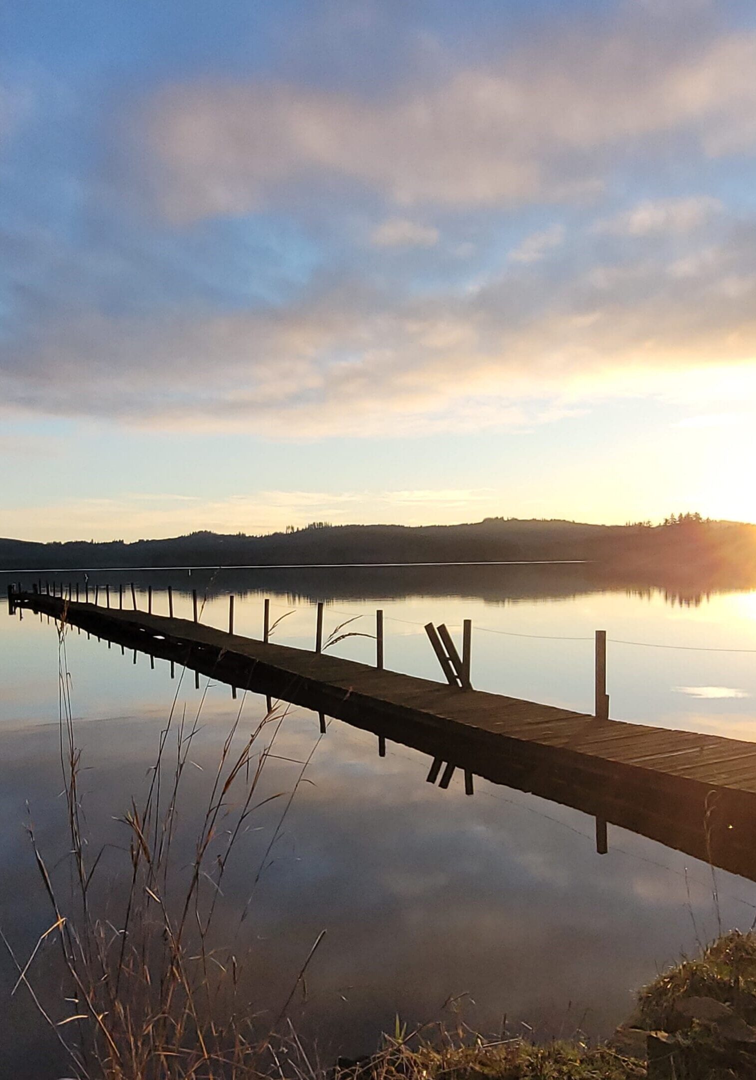 A dock on the water with sun setting in the background.